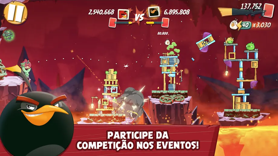 Pássaro vermelho junto à fisga à esquerda e torres de madeira com porcos à direita, num ecrã horizontal de Angry Birds 2